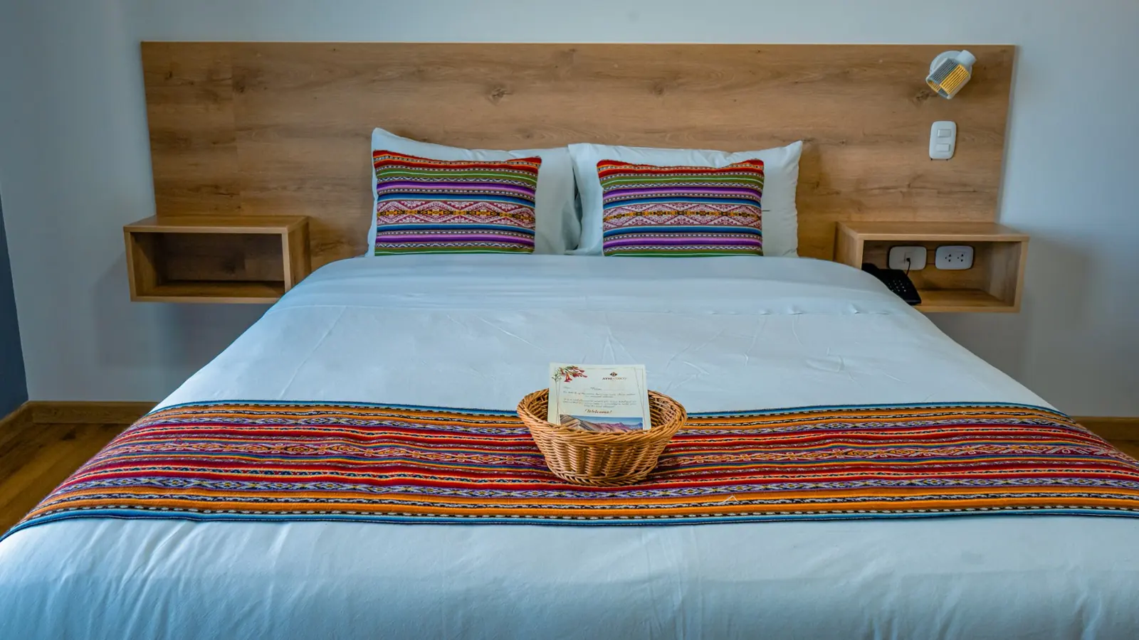 An Ayni bed with white linen, a wooden headboard and Andean textiles