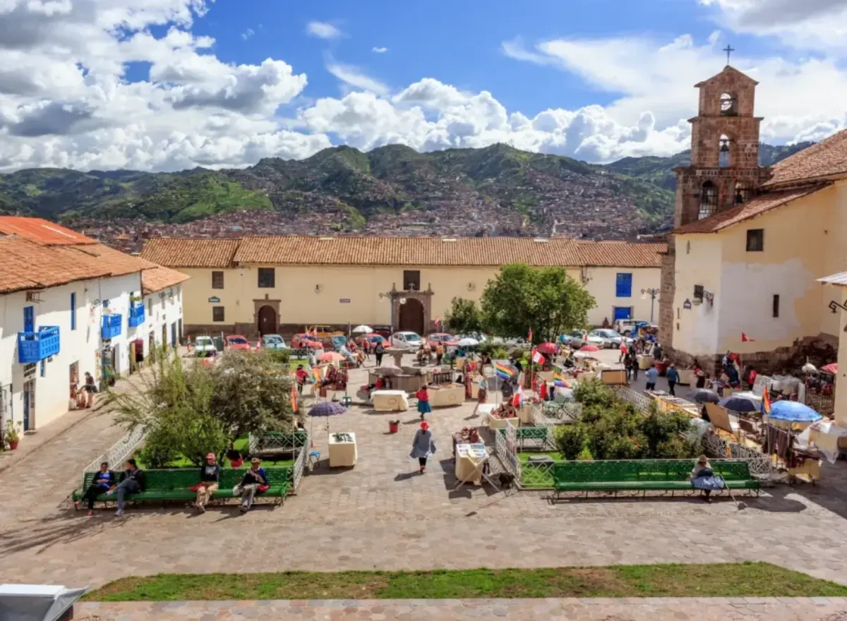 San Blas square in Cusco with a church, benches, visitors, mountains, and a traditional tourist setting.
