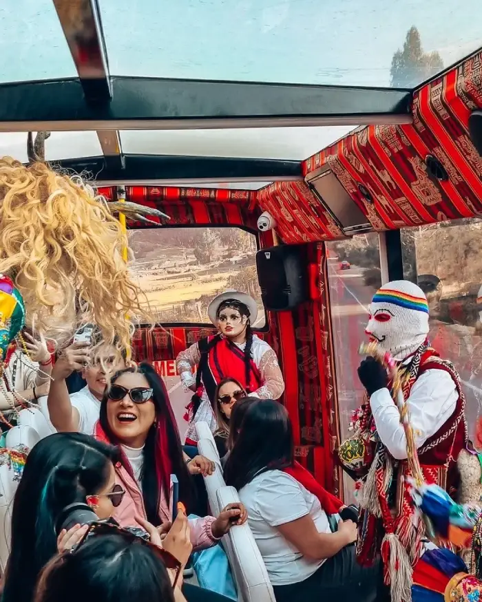 City tour en bus panorámico 180° en Cusco con turistas y personajes de danzas tradicionales durante el recorrido.