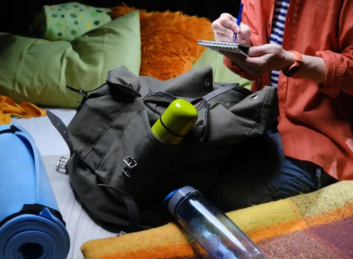Viajero preparando una mochila de día para Machu Picchu con botella de agua, libreta, ropa de abrigo y objetos personales.