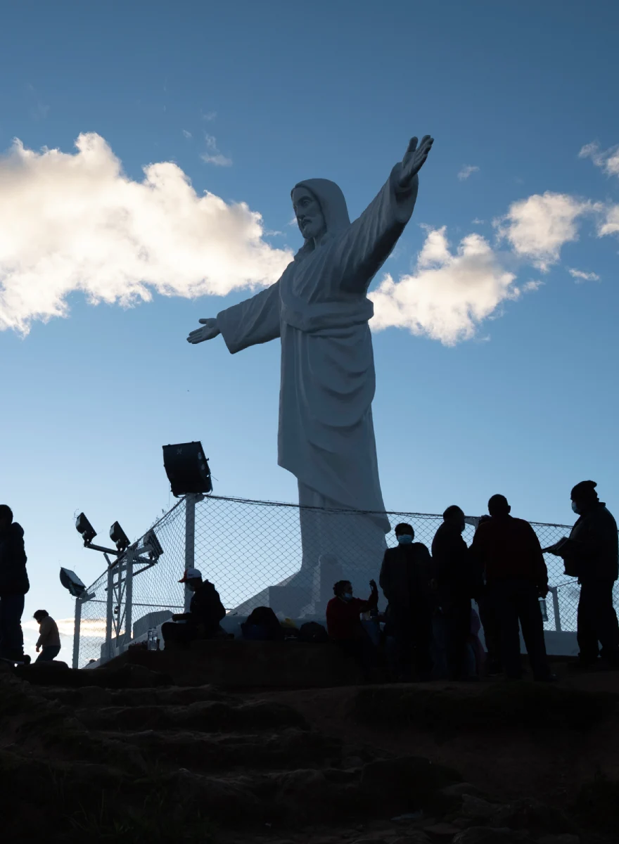 Mirador de Cristo Blanco en Cusco con estatua iluminada por el cielo, visitantes y vista elevada de la ciudad.