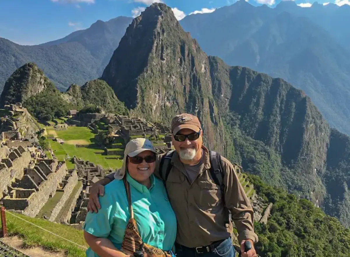Older couple at Machu Picchu with Andean mountains, Inca terraces, and clear scenery during their visit.