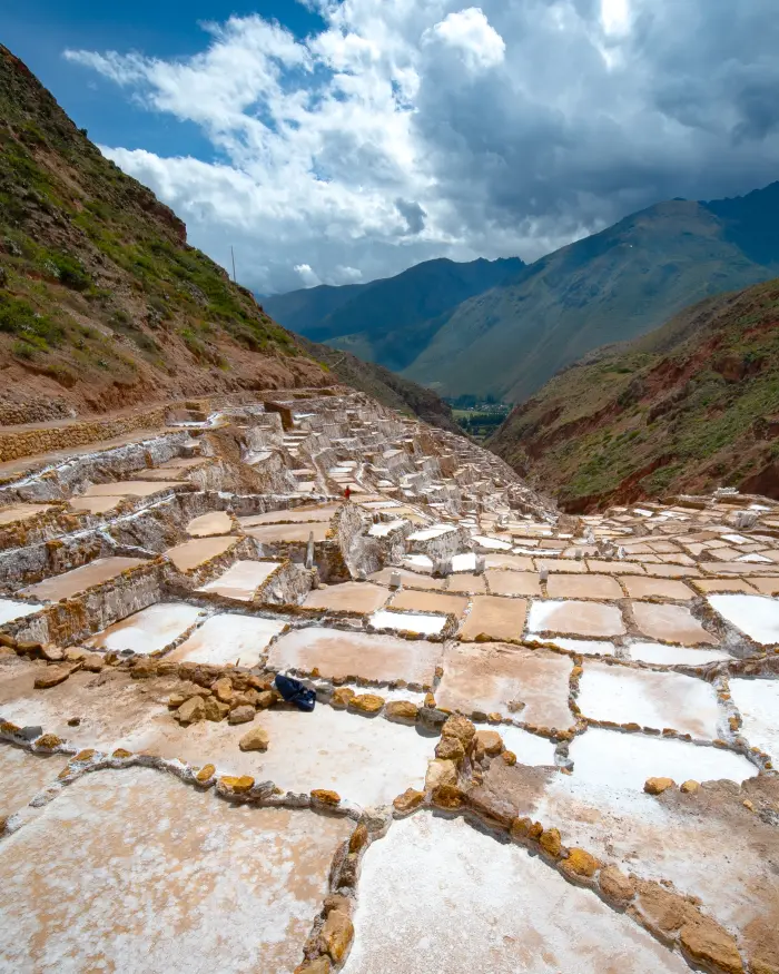 Salineras de Maras en Cusco con pozas de sal, montañas andinas, cielo nublado y paisaje del Valle Sagrado.