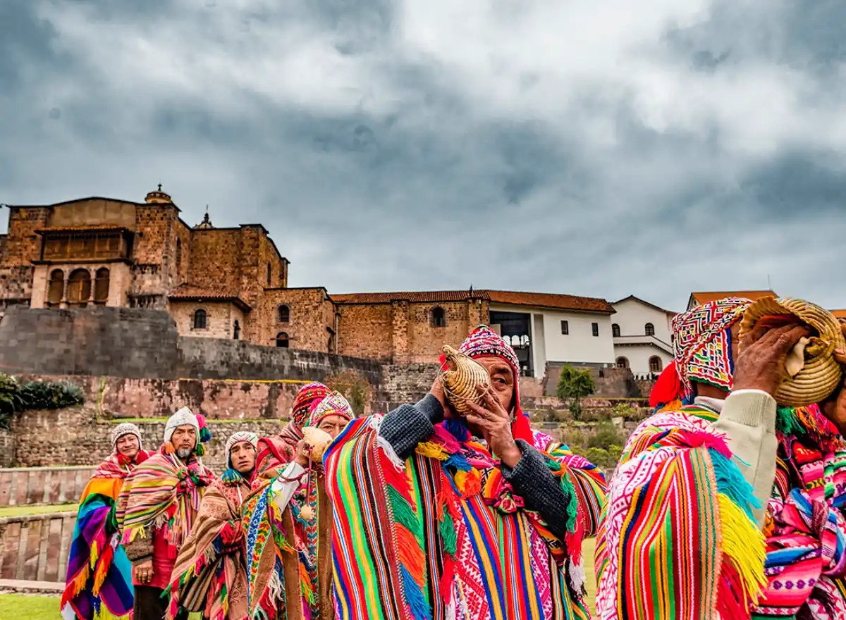 When to book a hotel in Cusco and how far in advance: Andean musicians wearing traditional ponchos playing pututus in front of a historic site.